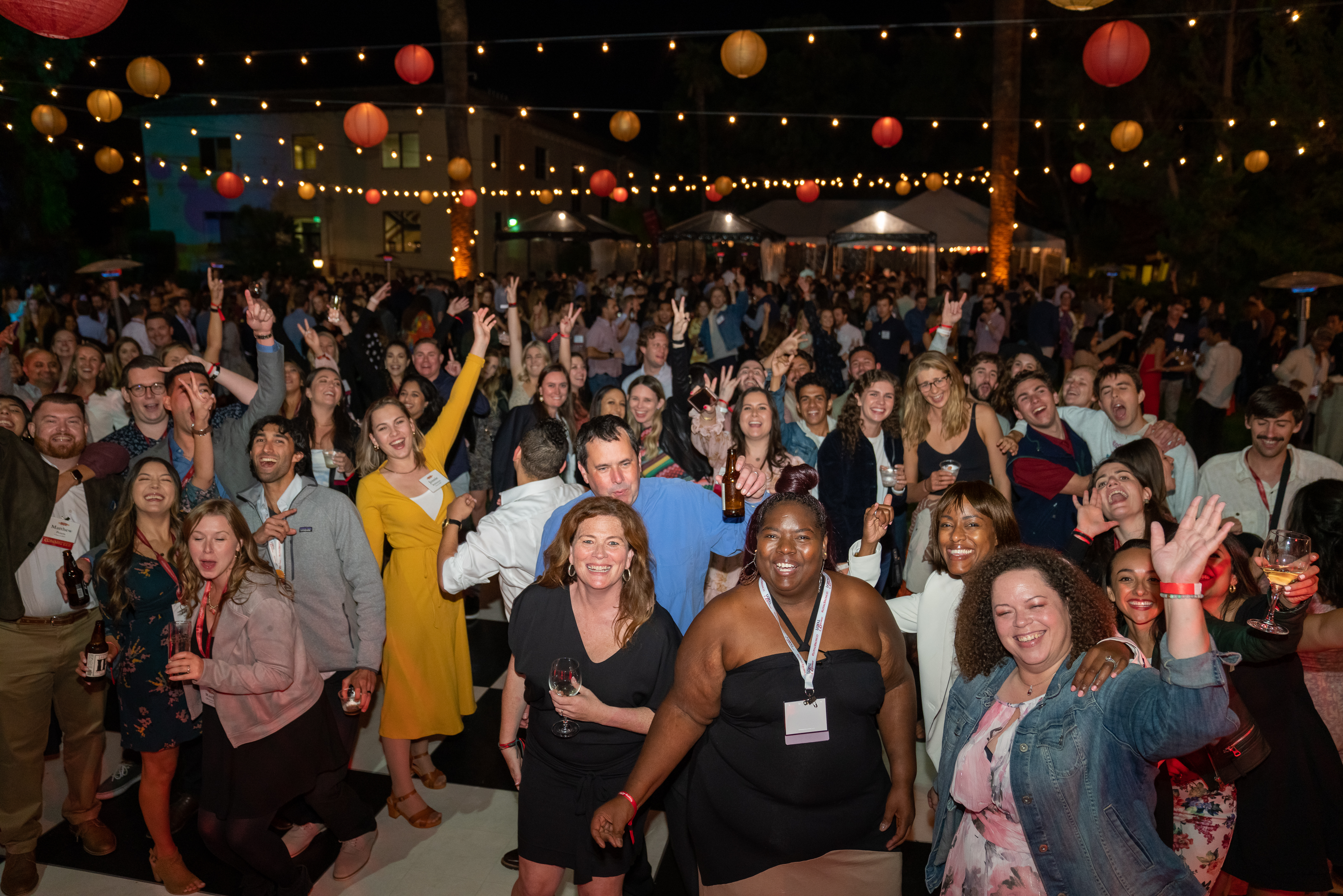 A large crowd dances under bistro lights and lanterns