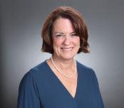 Alt text: Woman smiling in a headshot with a neutral gray background.