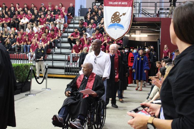 A person in a wheelchair is pushed by another during a graduation event.
