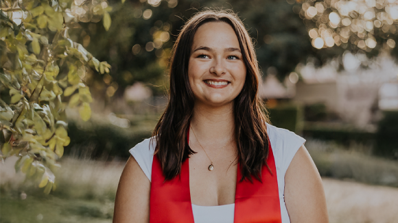 A smiling young woman wearing a white dress and a red commencement stole
