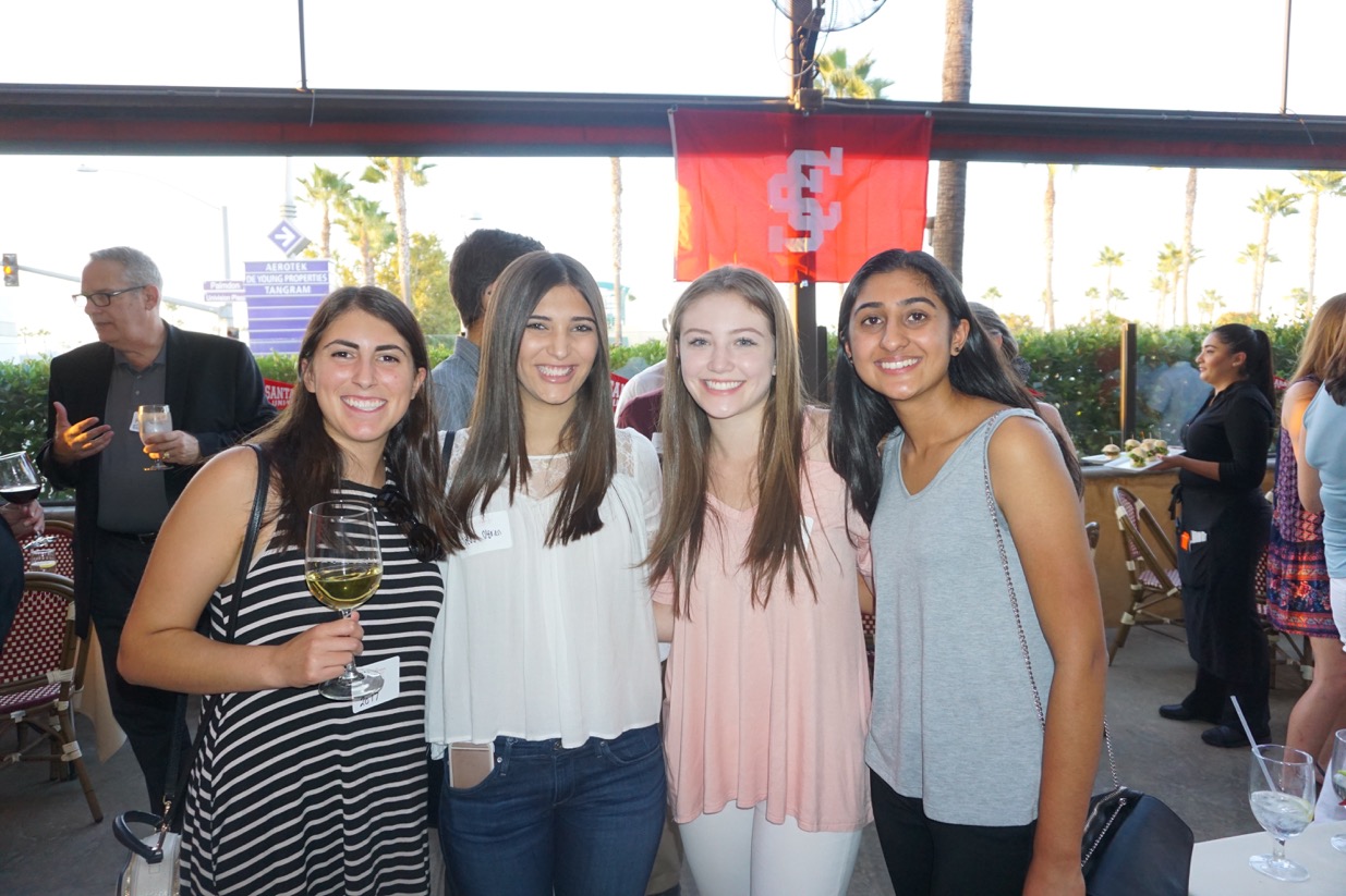 Four people smiling at an outdoor event in front of a red sign.