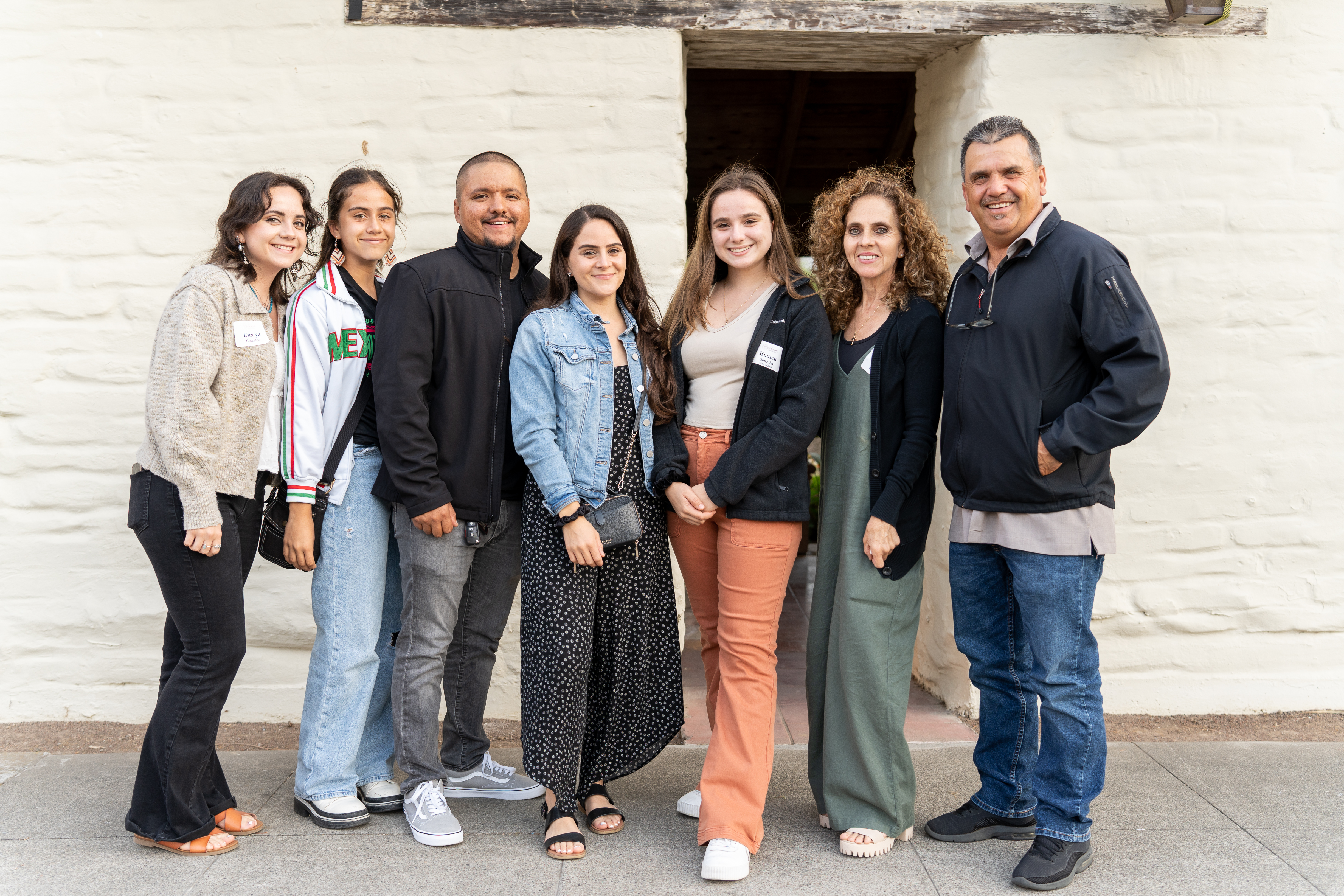 A group of seven people smiling and posing in front of a white wall.