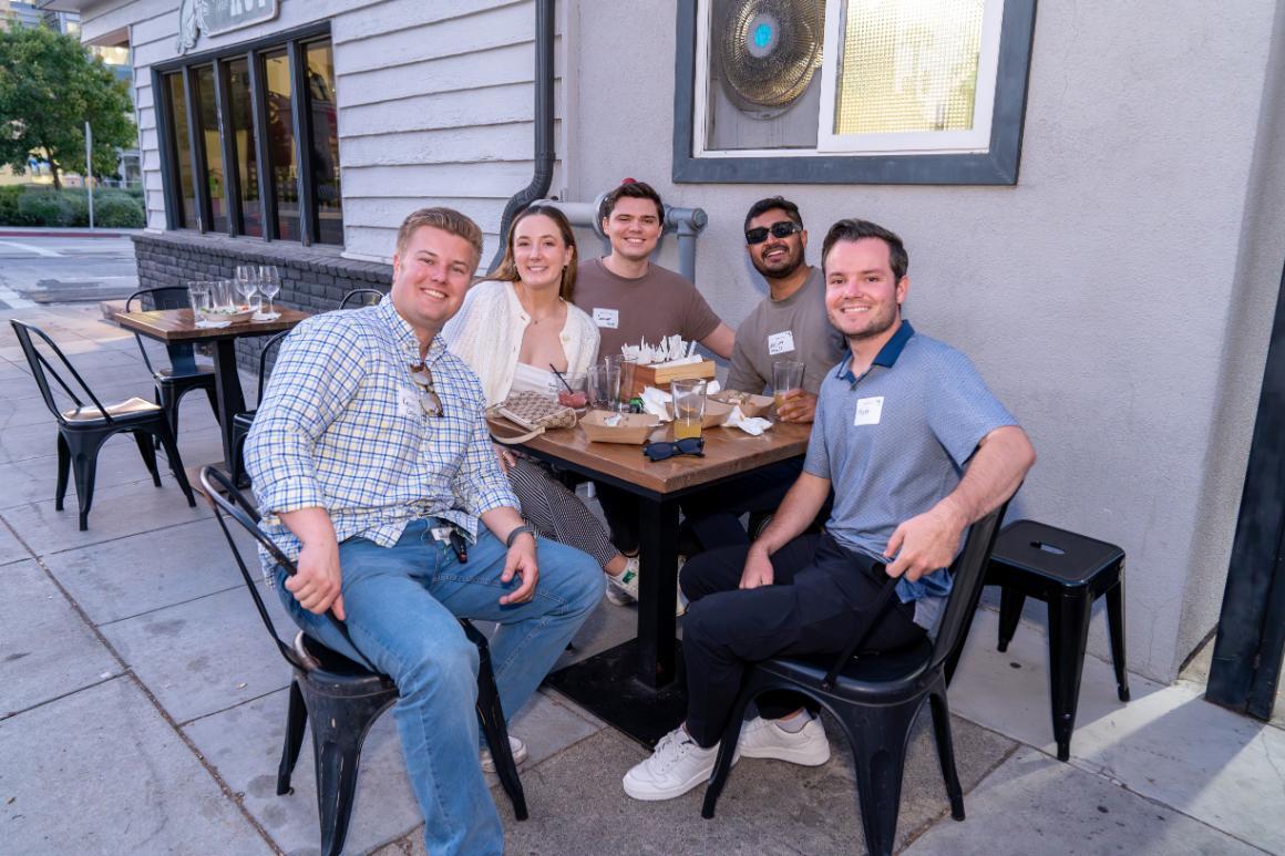 A group of smiling people sitting outside The Hut restaurant in Santa Clara, CA, USA.