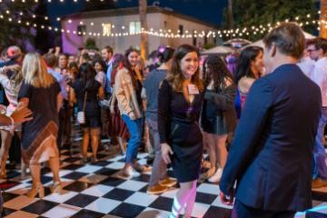 People mingling at an outdoor party with checkerboard flooring and string lights.