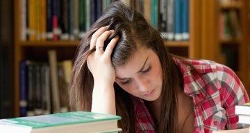A person in a library looking stressed with books around them.