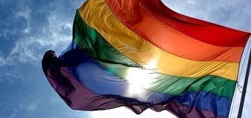 A waving rainbow flag against a blue sky.