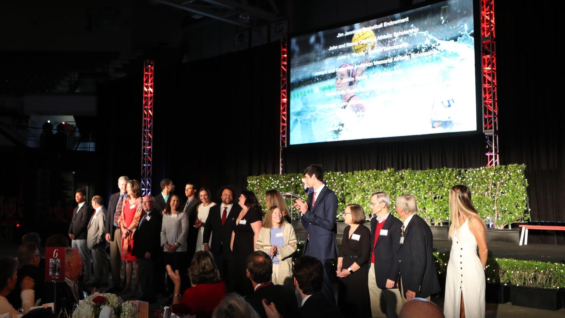 A group of people standing on a stage with a large screen behind them.