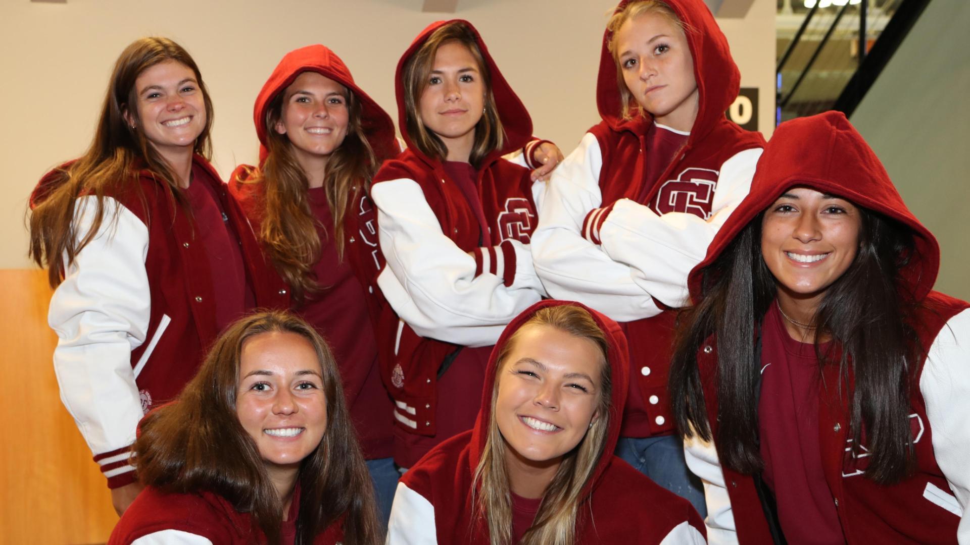 Seven people wearing letter jackets, with six of them smiling at the camera.