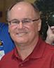 Man in red shirt holding two sink plungers with decorations and people in the background.