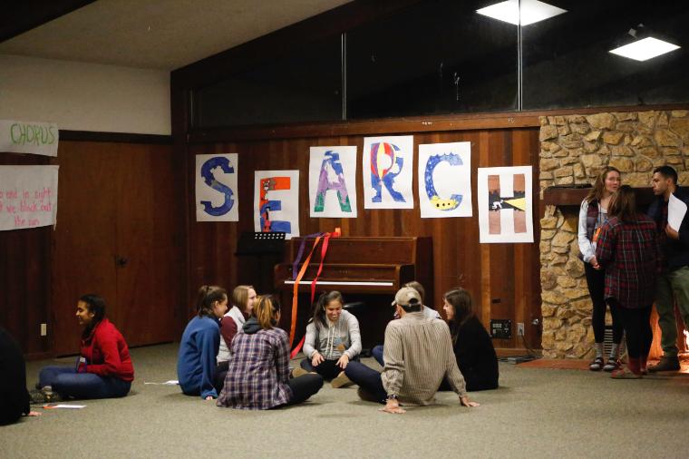 A group of people sitting on the floor with posters on the wall.