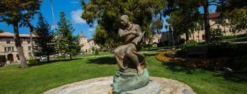 Bronze statue of a person on a pedestal amidst a park setting.