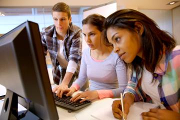 Three people, one man and two women, looking at a computer and working together