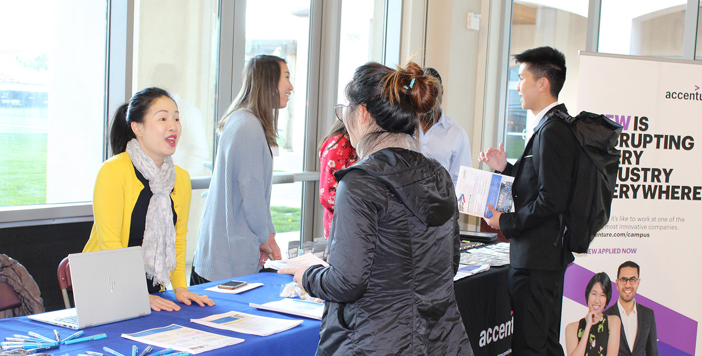 Alt text: People networking at a Diversity Works event with a blue table in the foreground.
