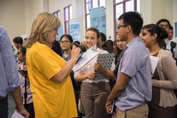 A group of people attentively listening to a woman in a yellow shirt.