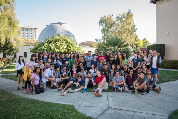 A large group of people pose outdoors in front of a building.