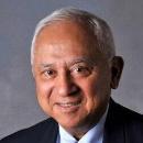 Older man smiling in formal attire against a grey background.