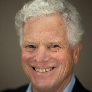 A man smiling, wearing a suit and a blue shirt.