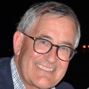 A person smiling and wearing glasses and a jacket.