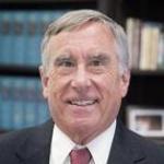 A man in a suit and red tie, smiling.