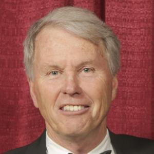 A person smiling in front of a red curtain.
