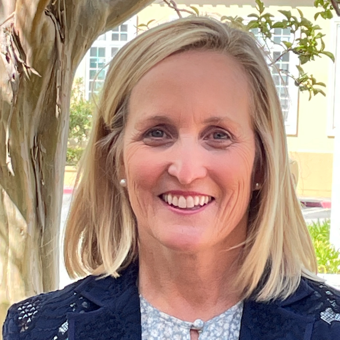 A woman smiling outdoors with trees in the background.