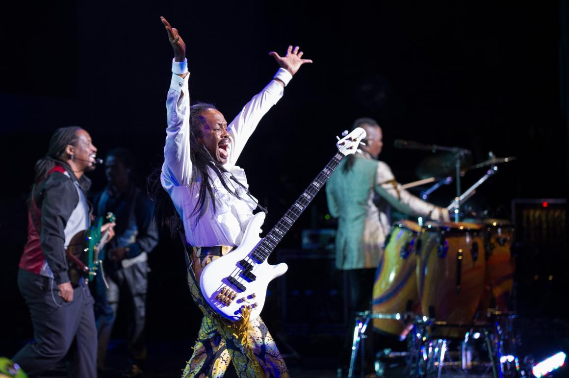 Band performing on stage; one member raises arm with guitar.