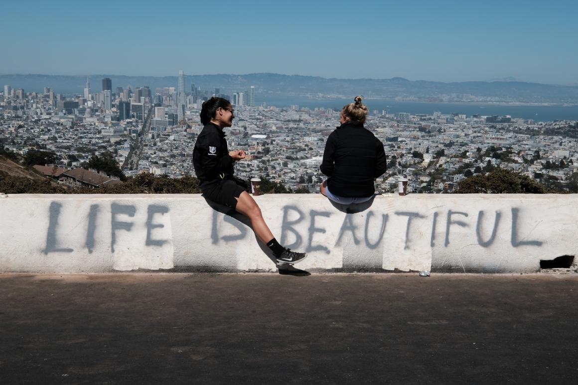 Photo of two people sitting on a barrier with the words