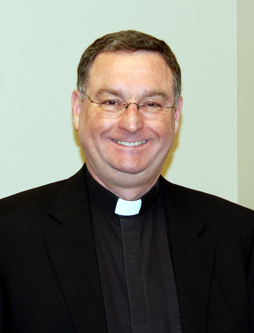 A person in clerical attire smiling in front of a light background. image link to story