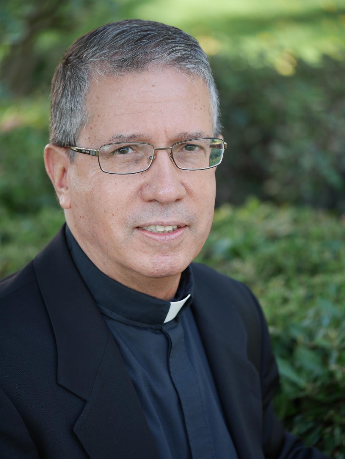 A man wearing clerical clothing with greenery in the background. image link to story
