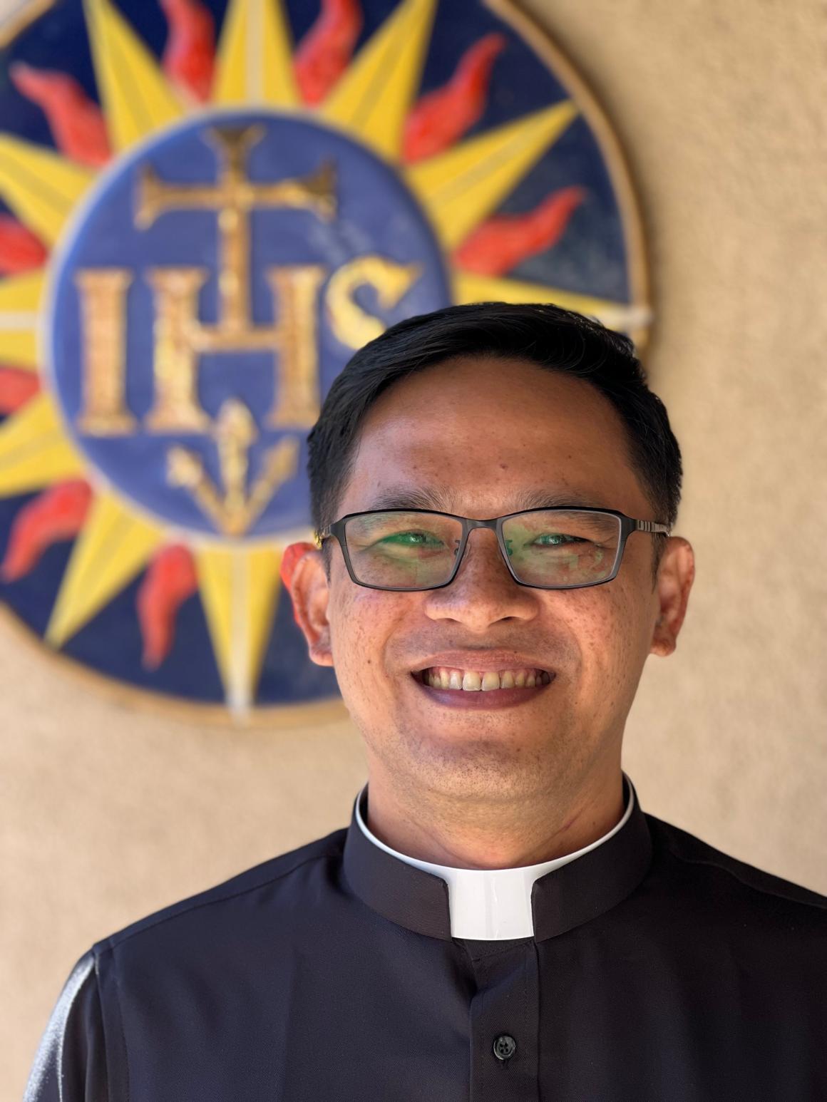 A man in clerical attire in front of a sunburst emblem. image link to story