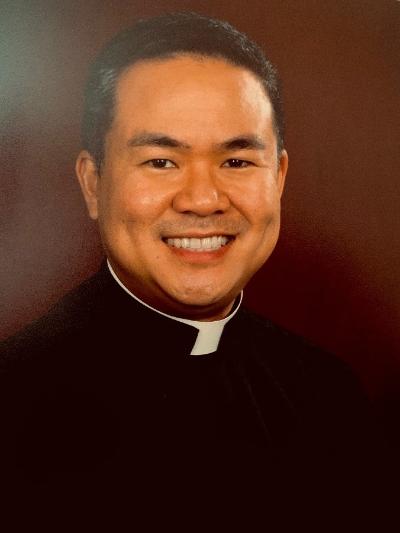 A man smiling, dressed in clerical attire against a dark background. image link to story