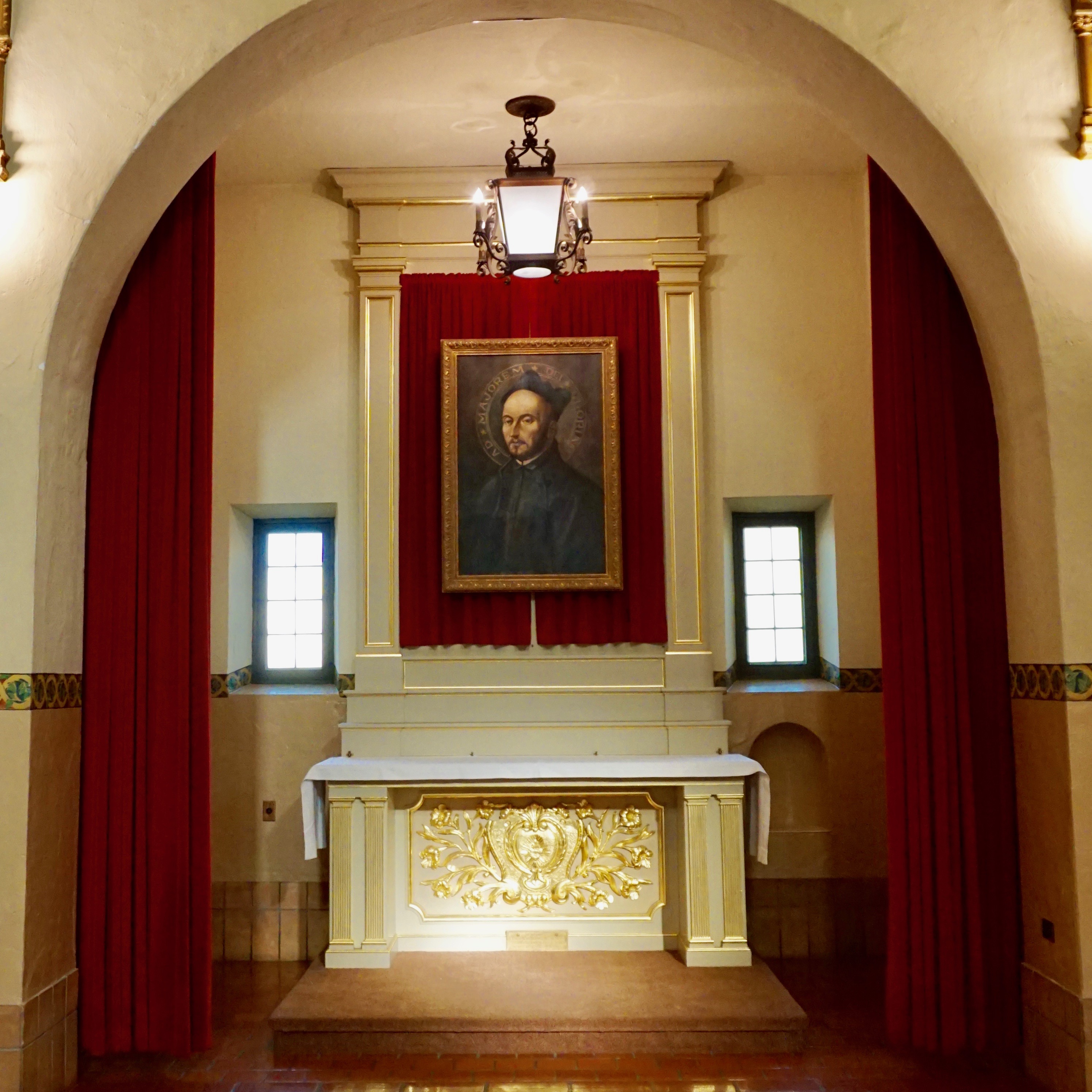 Alt text: St. Ignatius Side Chapel with altar, painting, and red curtains.