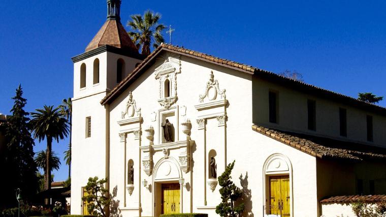 White mission-style church with bell tower under a clear blue sky.
