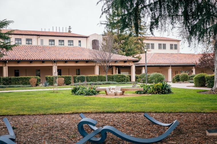 The exterior of Daily Science 300, a single story with a modern Adobe look. A bench and some pieces of modern art are visible next to the building.