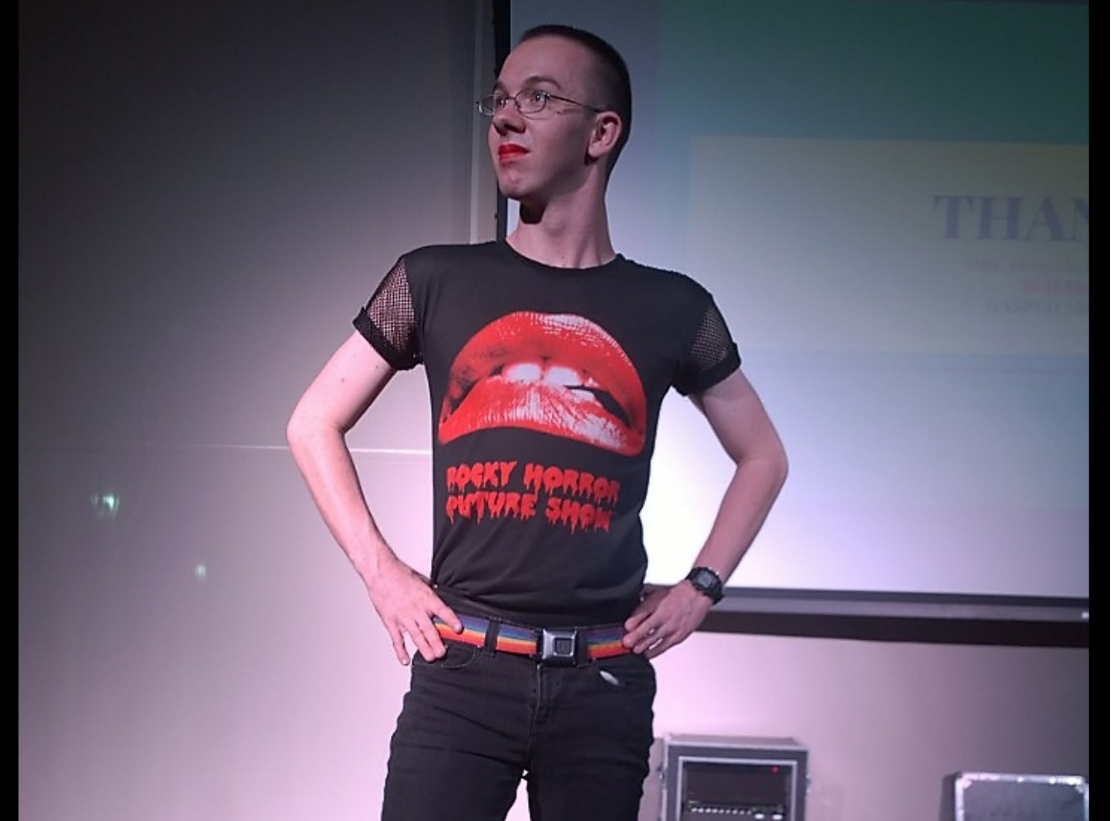 Person standing confidently on stage wearing a black shirt with a bold design.