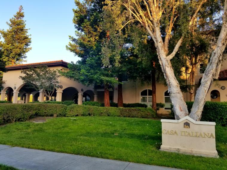 A beige building with green lawn and trees.