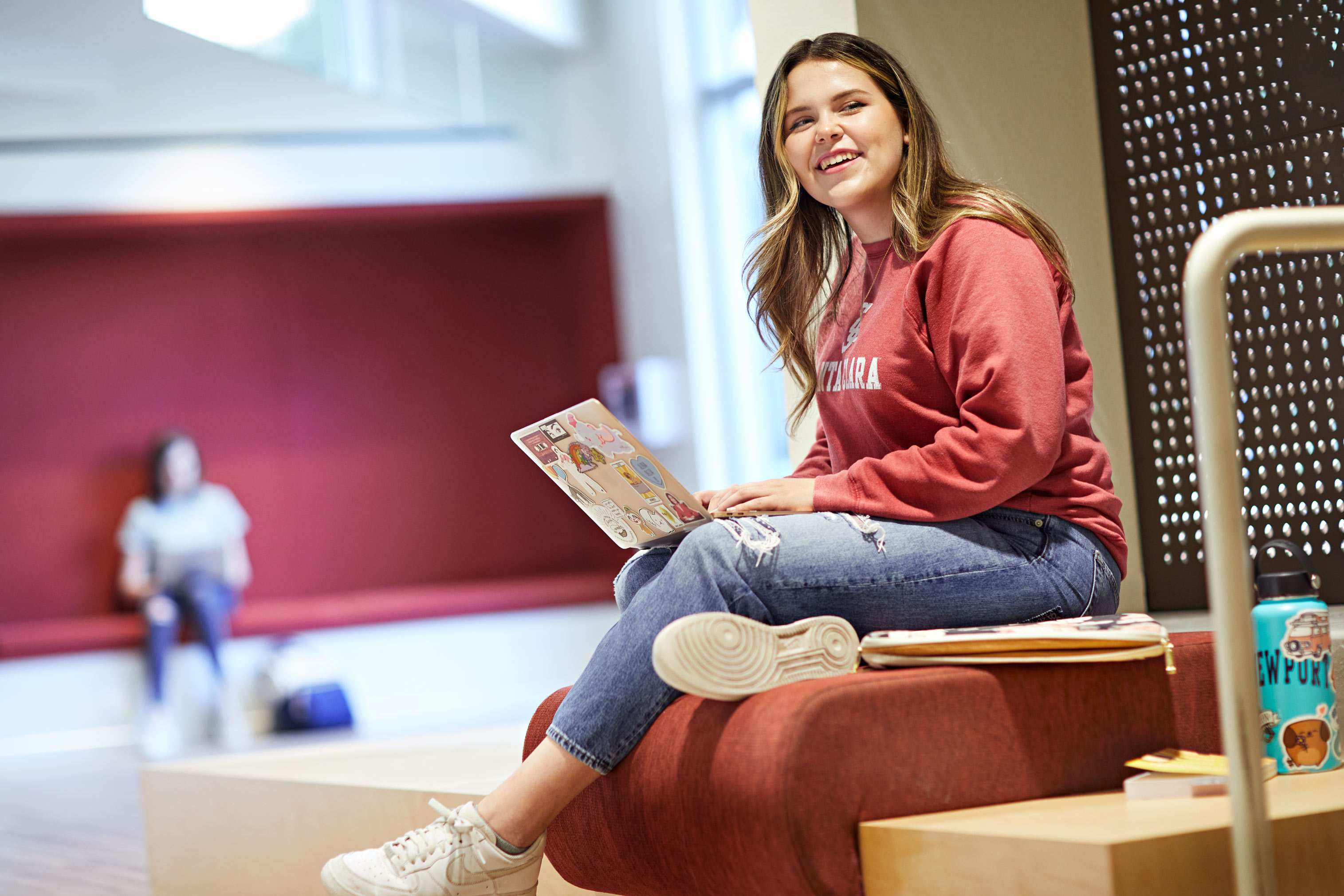 A person sits on steps with a laptop and smiles.