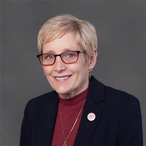 A person wearing glasses and a dark blazer, smiling.