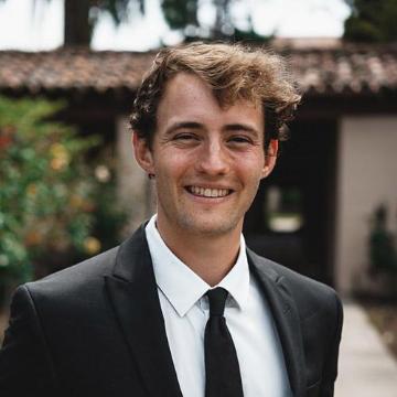 A man in a suit smiling outdoors.