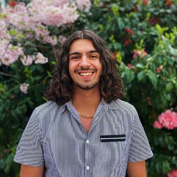 A person smiling in front of blooming flowers.