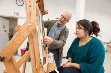 A teacher instructing a student in an art class, using an easel.
