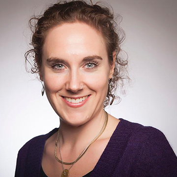 A person smiling, wearing a purple top and necklace. 