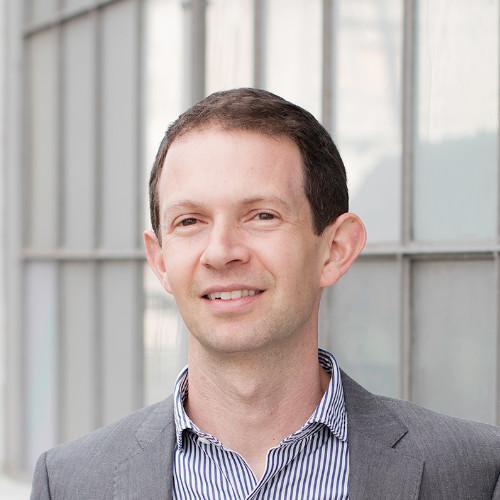 A person smiling in front of a modern glass building.