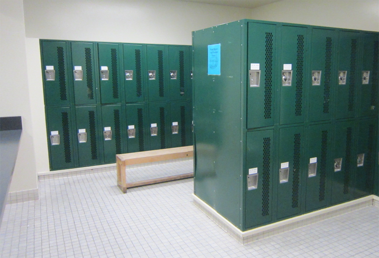 A locker room with green lockers and a wooden bench.