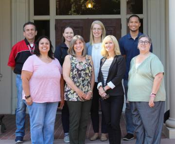 Group photo of eight people standing in front of a building.
