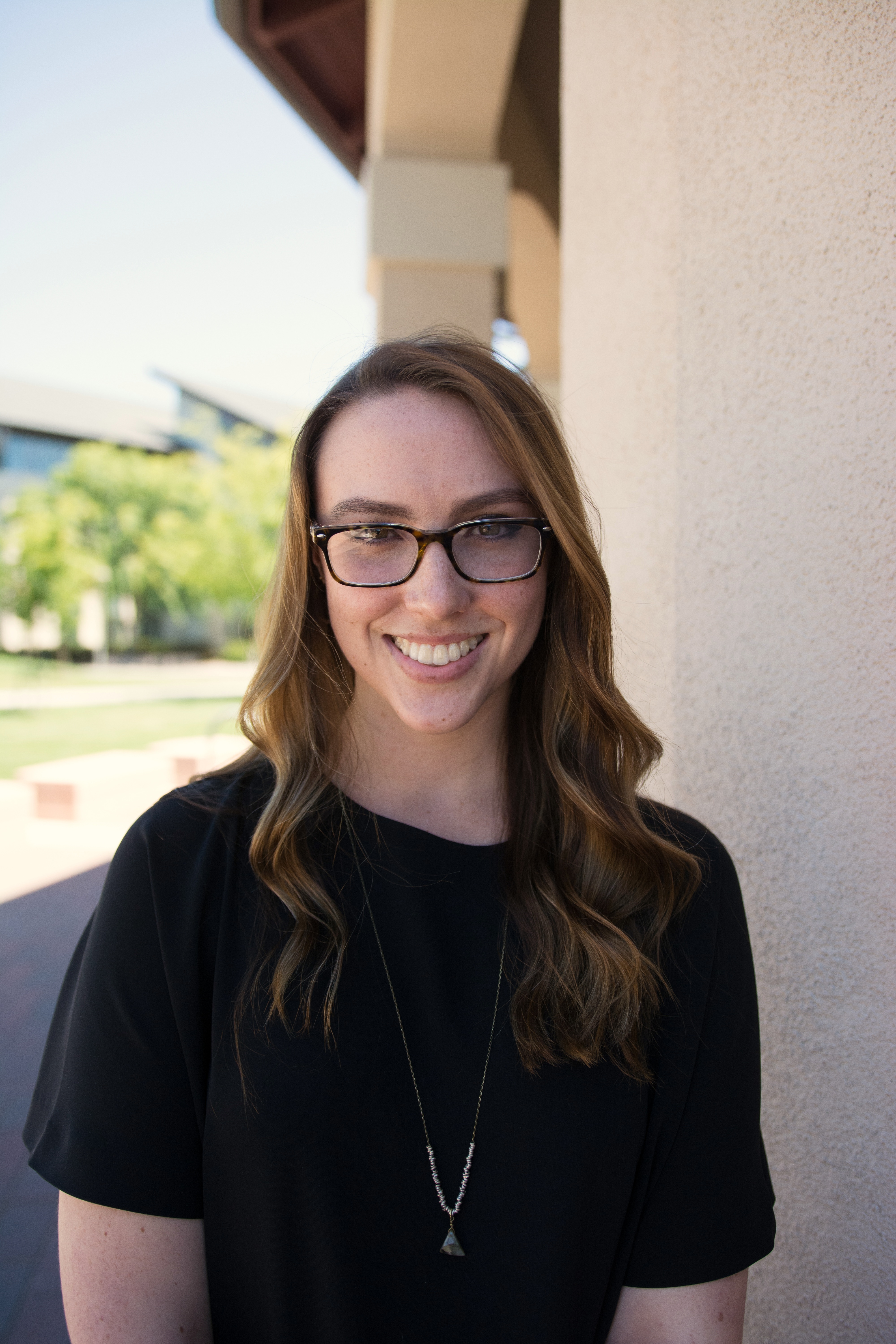 A person wearing glasses and a black shirt standing outside a building.