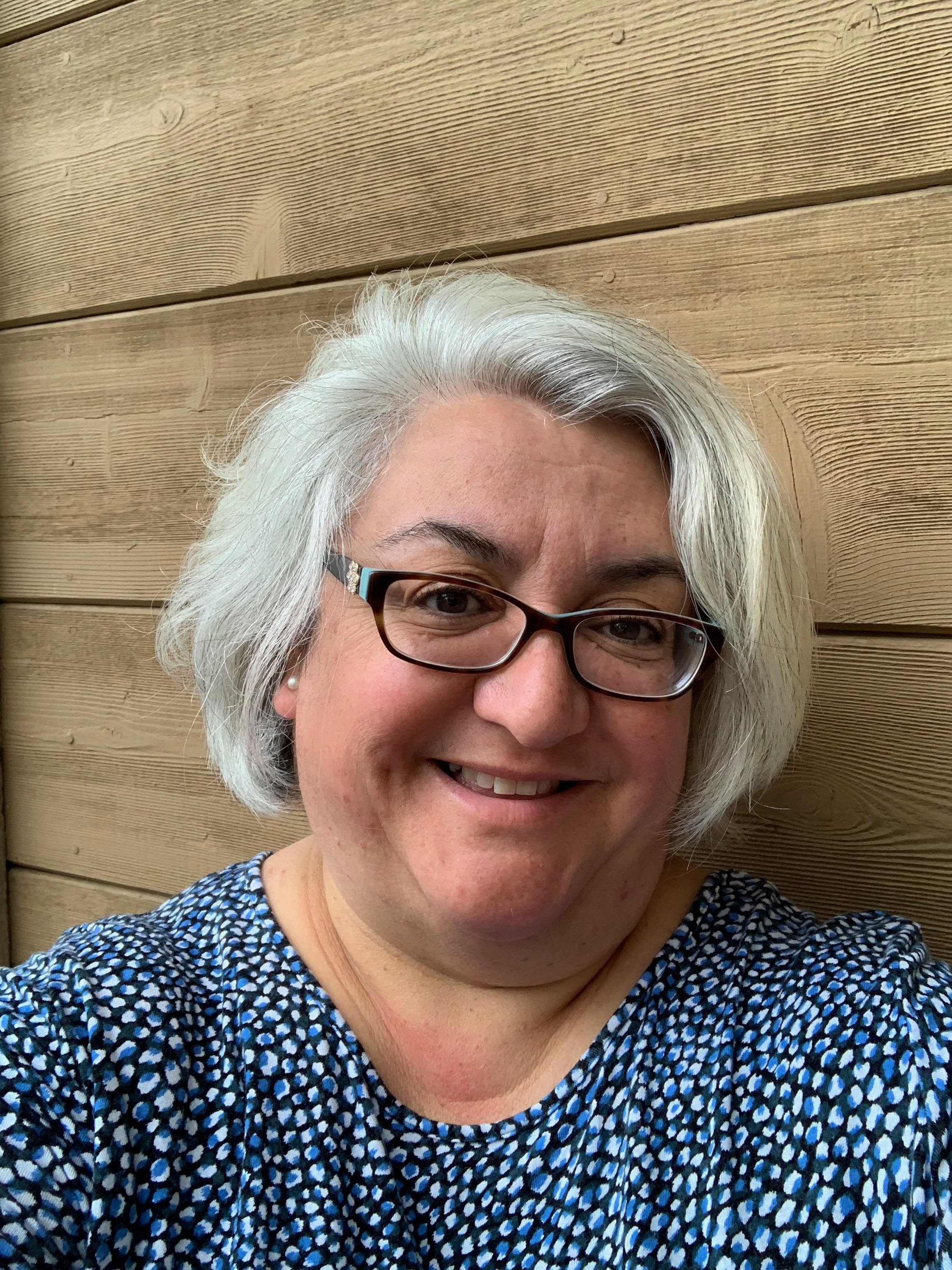 A person wearing glasses, smiling, in front of a wooden background.