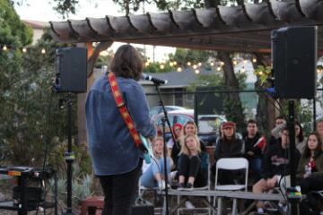 The back of someone singing and playing guitar to an audience in the forge