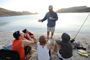 A group of people seated outdoors listening to a standing person.