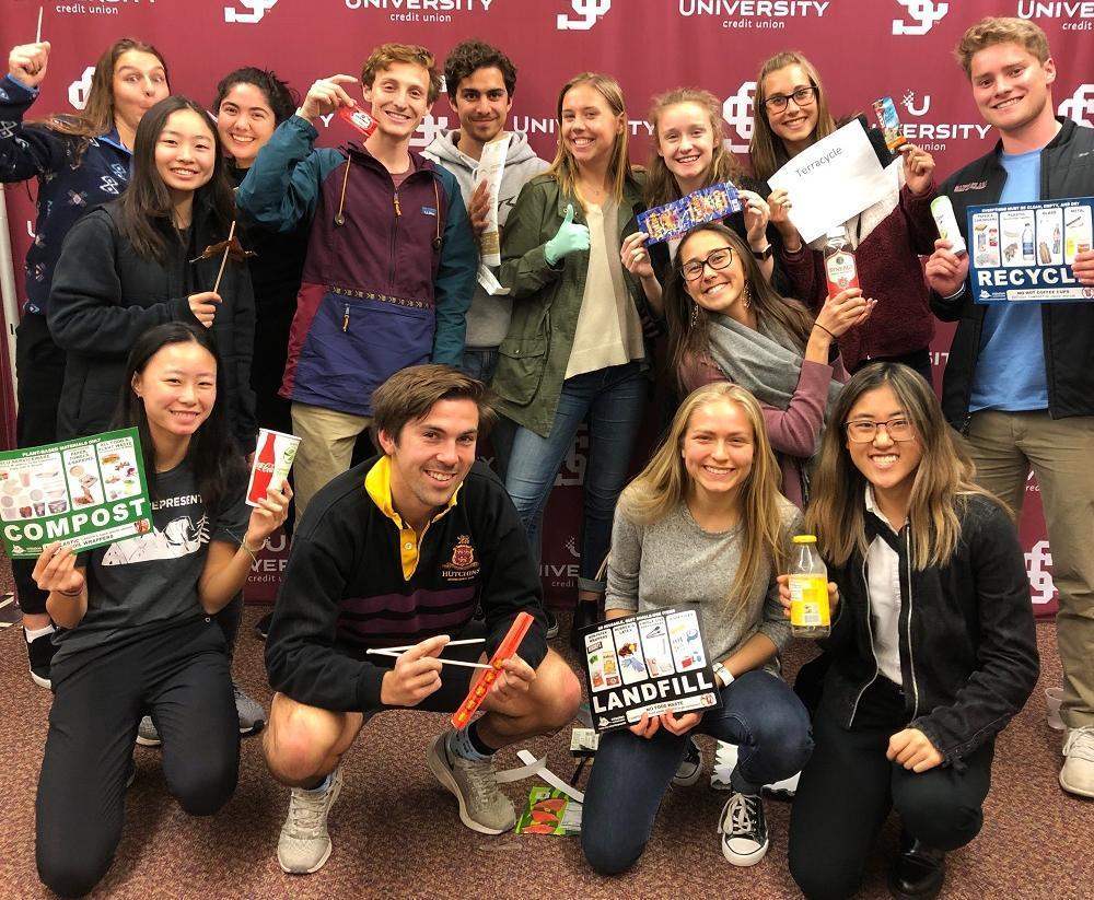 Student group smiling and holding up waste sorting signage  